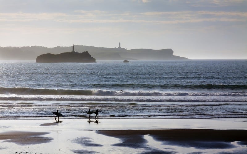 Surferos pasean a orillas de la playa de Somo
