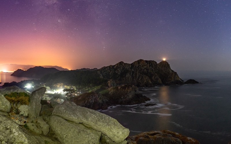 Panorámica de la isla de noche, y un faro brillando bajo las estrellas
