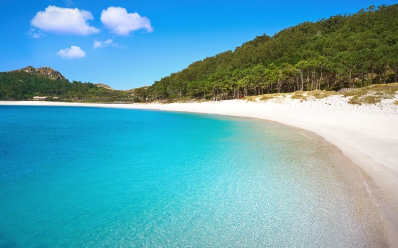 Una playa de aguas turquesa y arenas blancas, enmarcada entre bosques