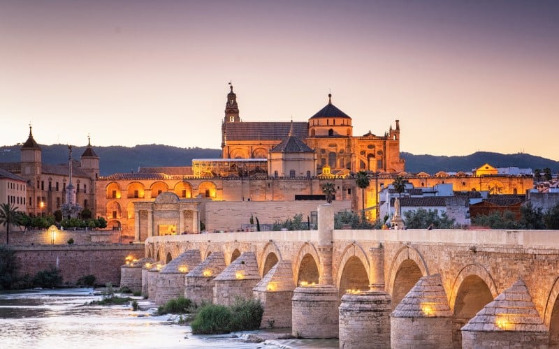 Un puente sobre un río y una ciudad iluminada al atardecer