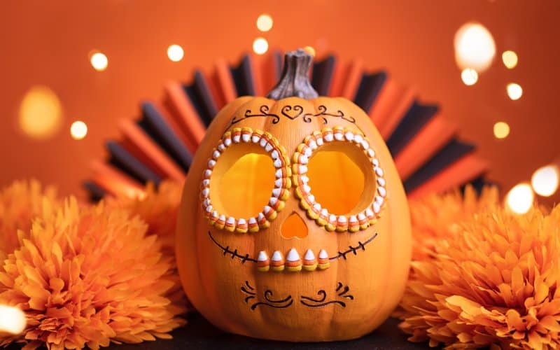 Una calabaza rodeada de flores y decorada con motivos mexicanos