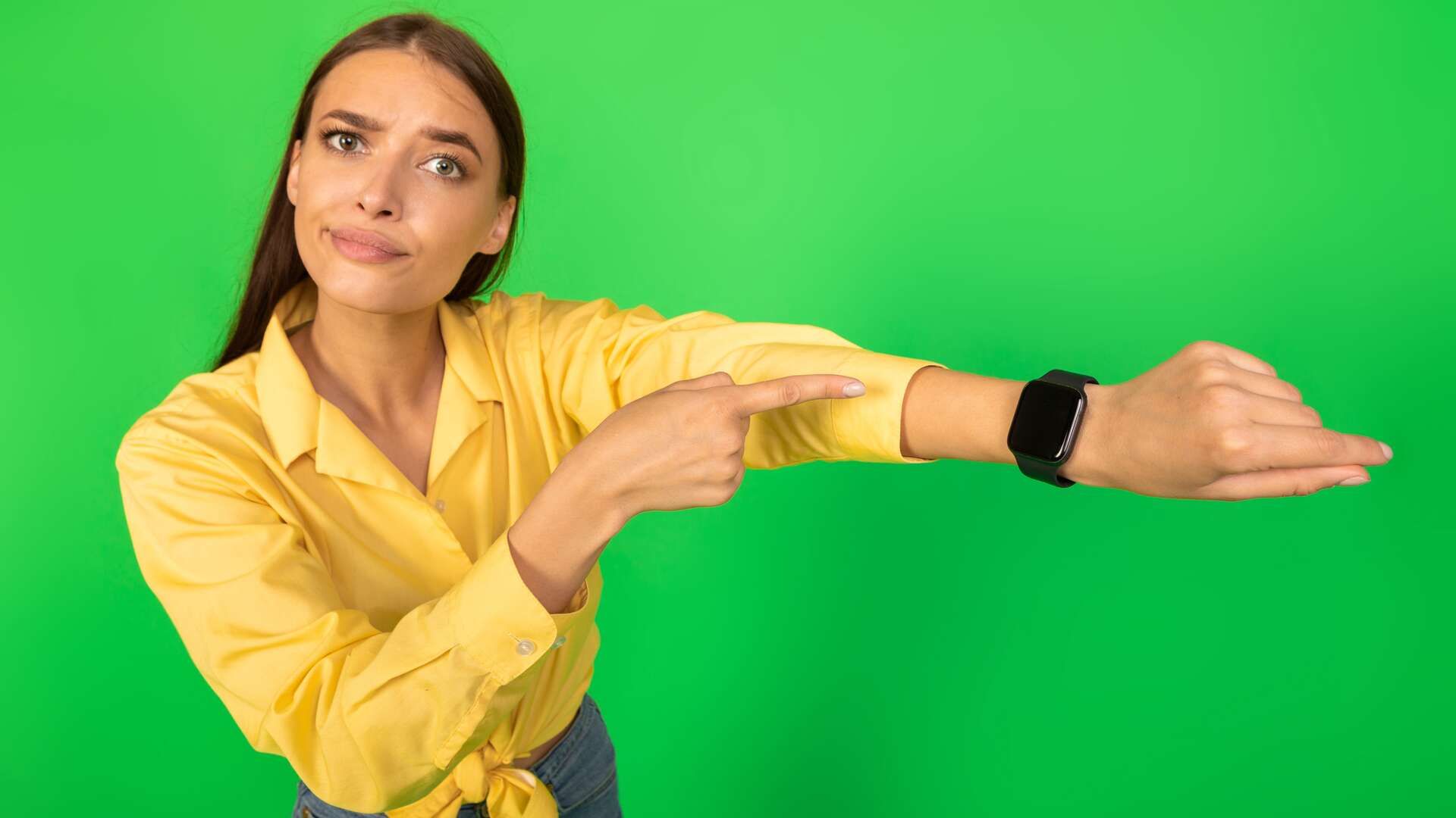 Discontented Woman Pointing Finger At Smartwatch Standing Over Green Background